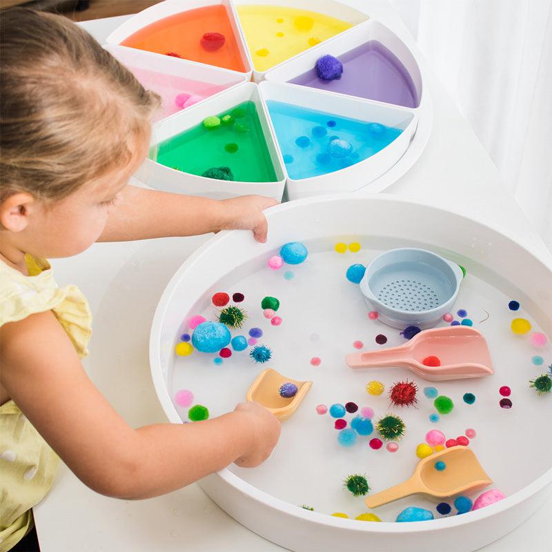 Child playing with scoops, pompoms, and coloured water in the play tray