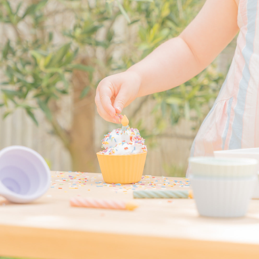 Child sprinkling colourful sprinkles onto sensory play cupcakes 