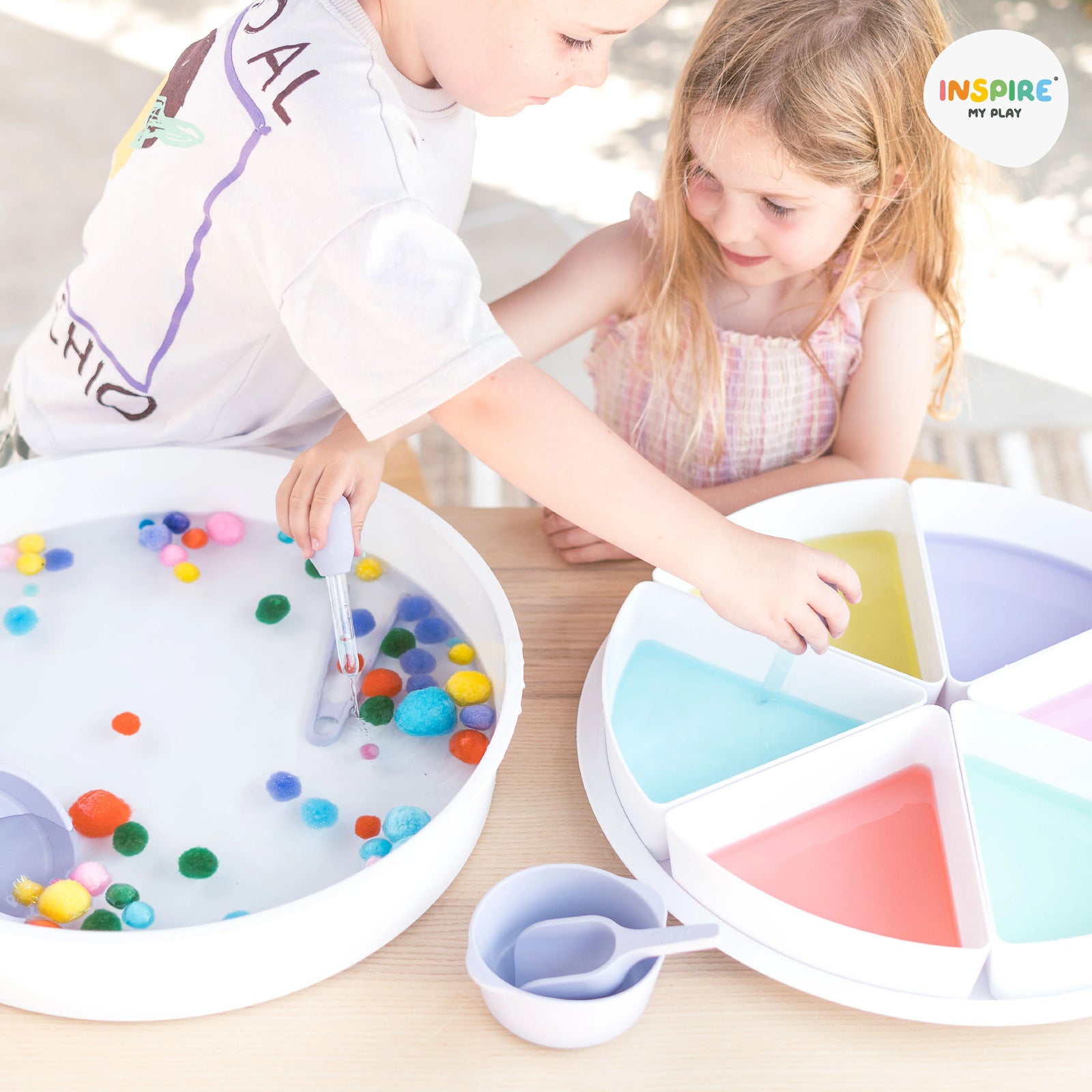 Two children sorting pom poms by colour in PlayTRAY filled with water