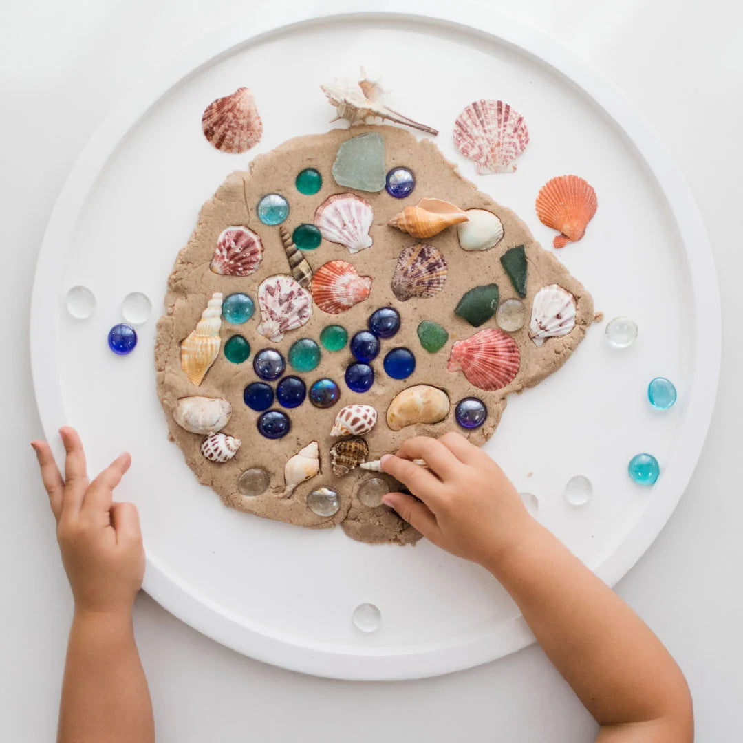 Child pressing shells into Playdough on PlayTRAY lid
