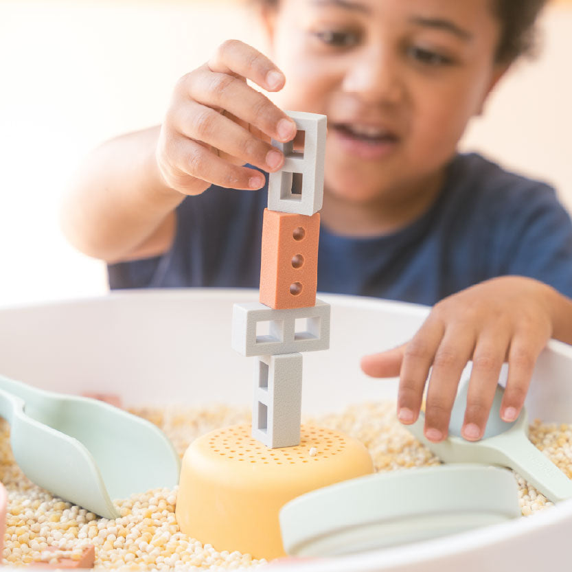 Young child building a tower with bricks and blocks during sensory play using the PlayTRAY
