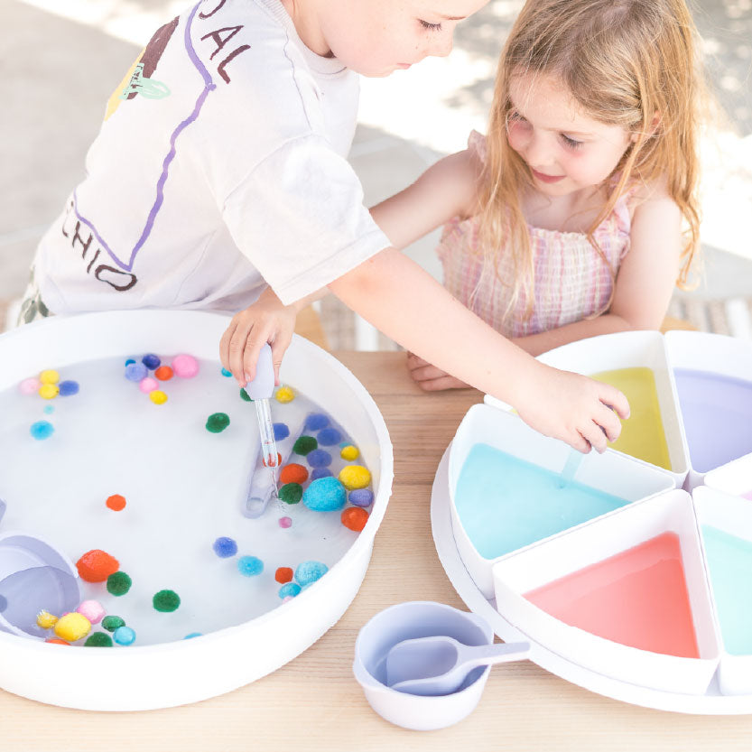 Two children sorting pom poms by colour in PlayTRAY filled with water