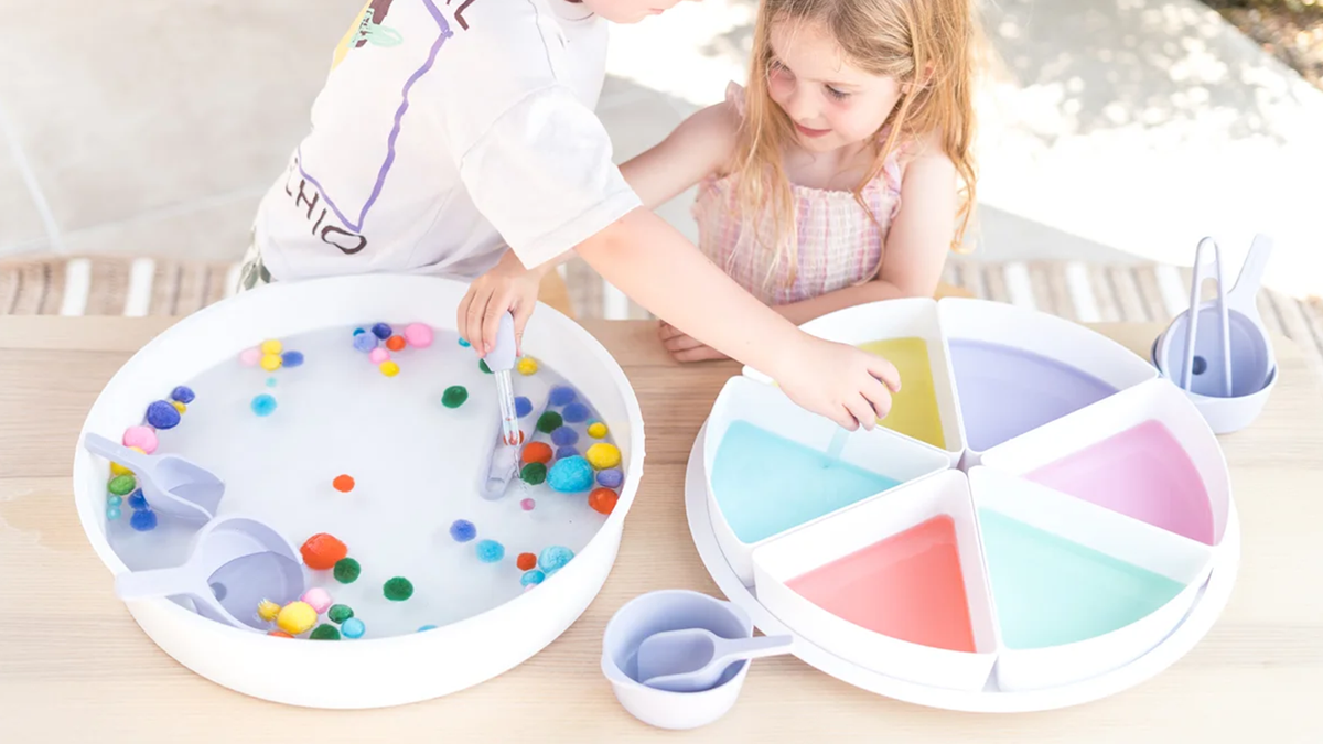 Two children playing outside with an Inspire My Play sensory play PlayTRAY filled with water and sensory play tools.