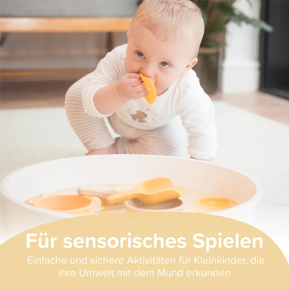 Baby playing with a yellow object in a play tray, with text about taste-safe sensory play.