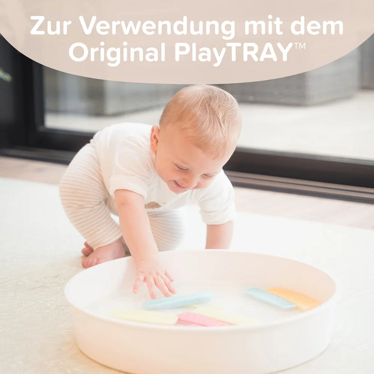 Baby playing with colourful foam strips in a round play tray indoors.