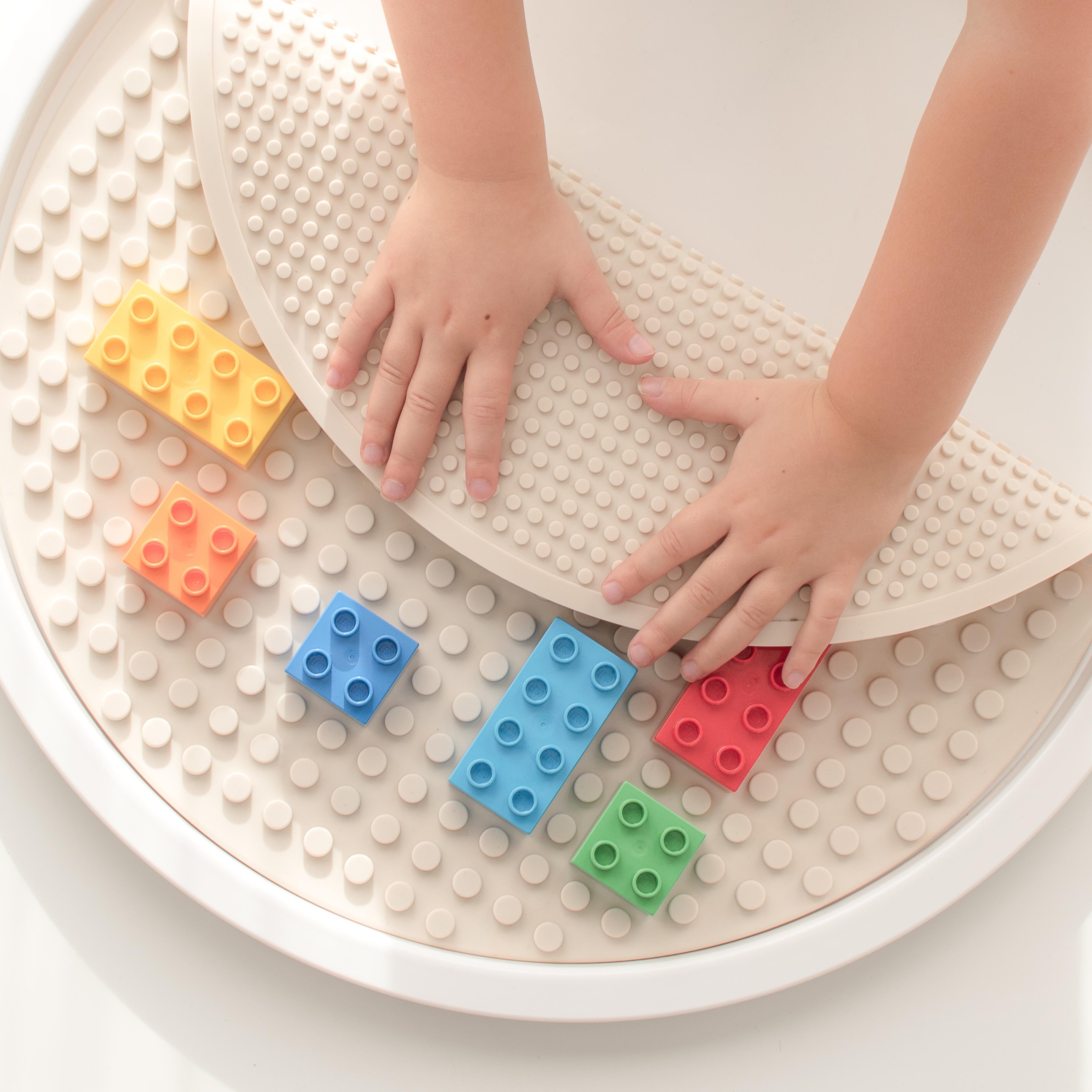 Children's hands interacting with colourful building blocks on a stone coloured building block mat/baseplate in the lid of a PlayTRAY.