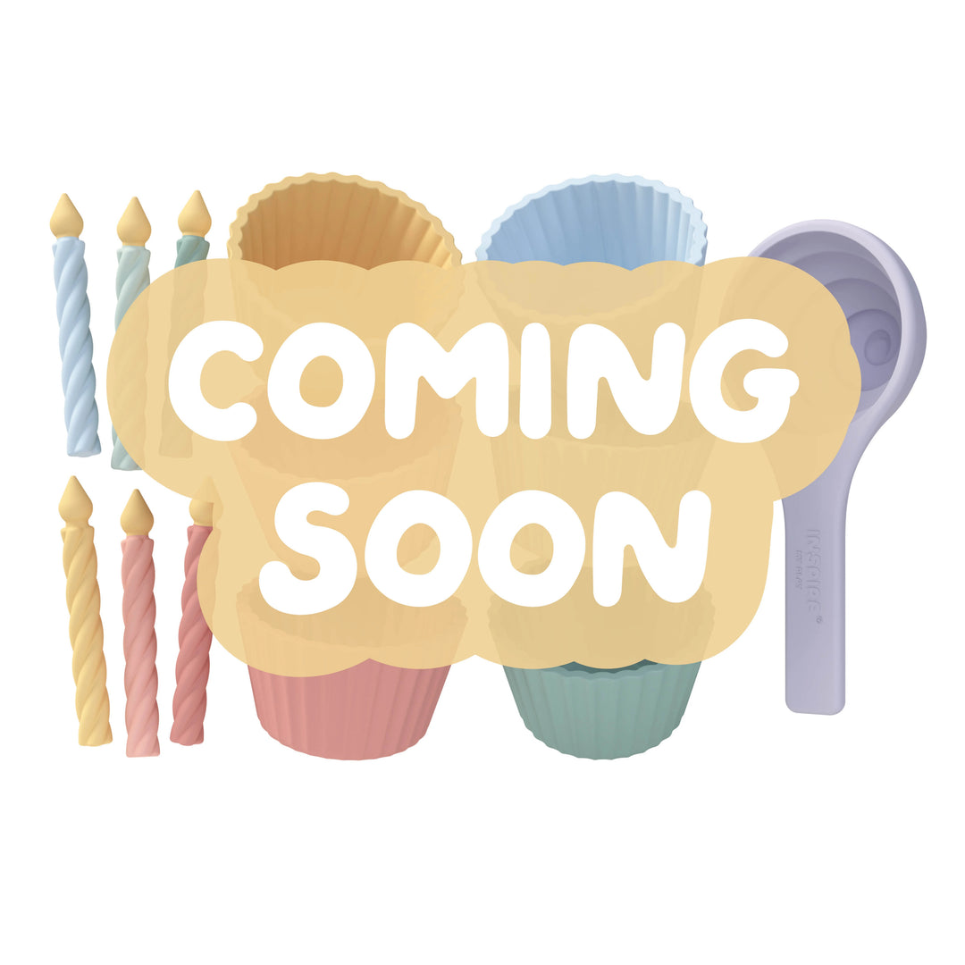 A digital graphic with a large beige cloud-shaped overlay reading 'COMING SOON' in white rounded letters. Behind the text are pastel-coloured cupcake cases, candles and a scoop on a plain white background.