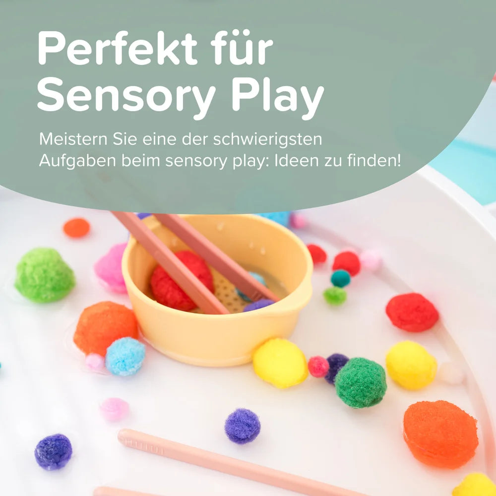 Pom poms floating in water in a play tray alongside a bowl and a set of tweezers