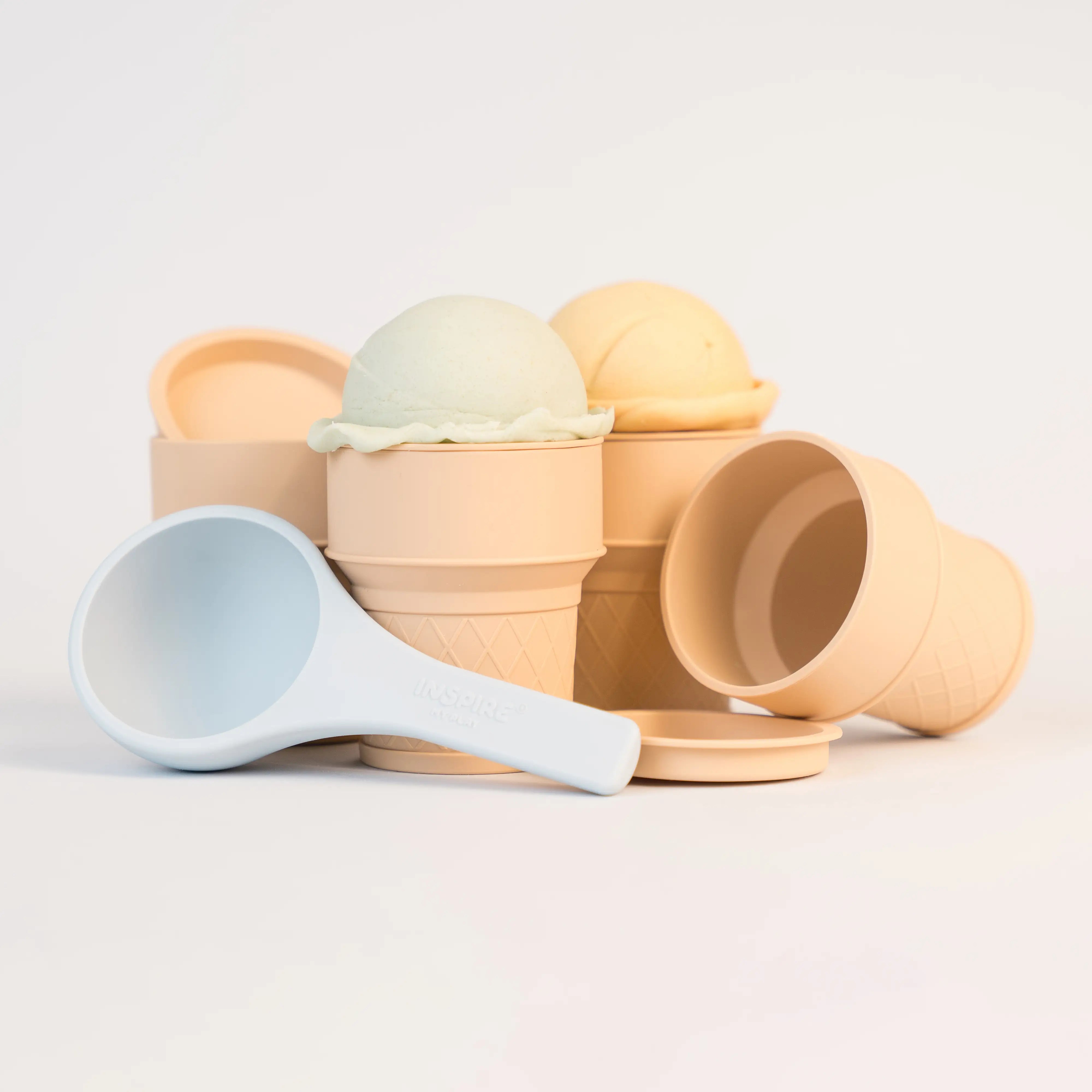 A set of beige toy ice cream cones with matching coloured lids and a blue silicone scoop. The ice cream cones are topped with sensory material. 