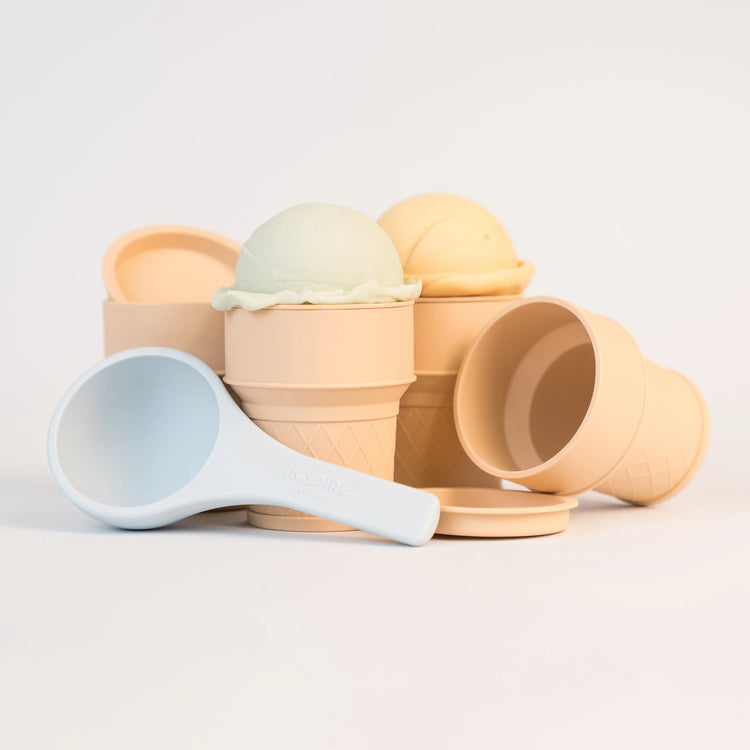A set of beige toy ice cream cones with matching coloured lids and a blue silicone scoop. The ice cream cones are topped with sensory material. 