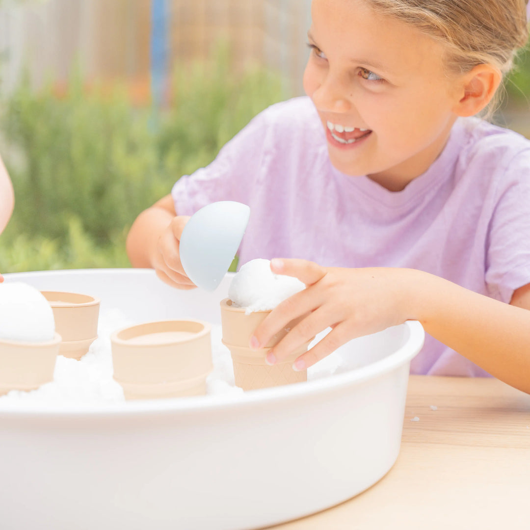 Child scooping artificial snow into a toy silicone ice cream cone in the PlayTRAY.