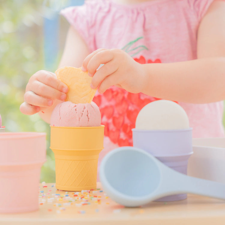 Child's hands placing a wafer in a silicone toy ice cream cone with a blue scoop in the foreground.