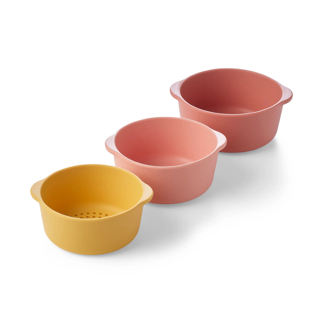 Three round silicone sensory play nesting bowls for children including one sieve bowl in yellow, pink and coral arranged diagonally on a white background.