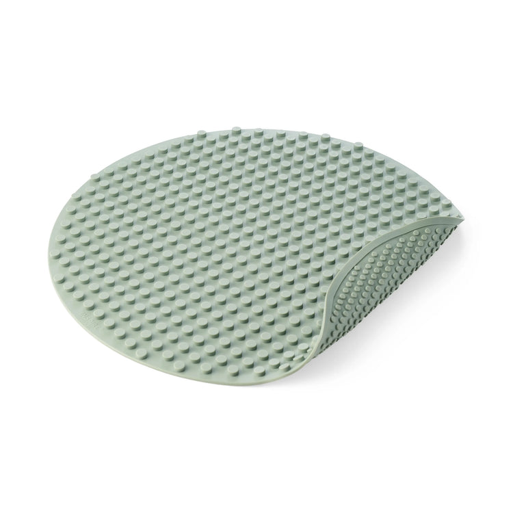 An oval-shaped sage green silicone building block mat for children's construction play with a raised textured pattern, shown on a clean white background with one corner folded over.