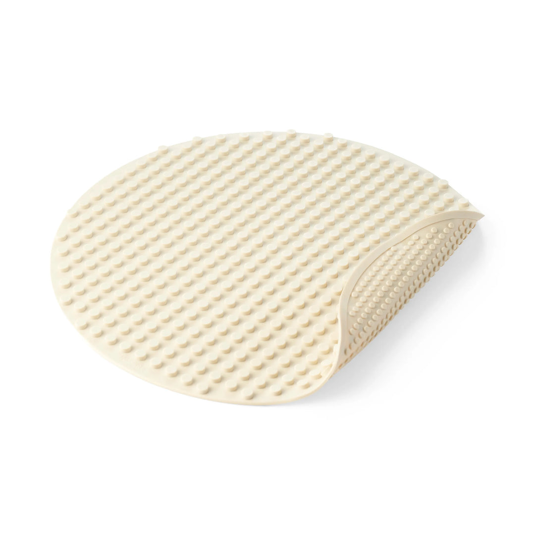 An oval-shaped beige silicone building block mat for children's construction play with a raised textured pattern, shown on a clean white background with one corner folded over.