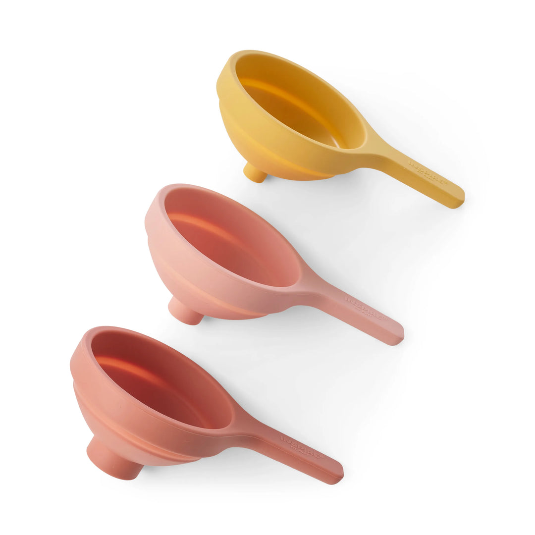 Three silicone collapsible funnels for sensory play, sand play and water play in coral, pink and yellow shades arranged diagonally on a clean white background.