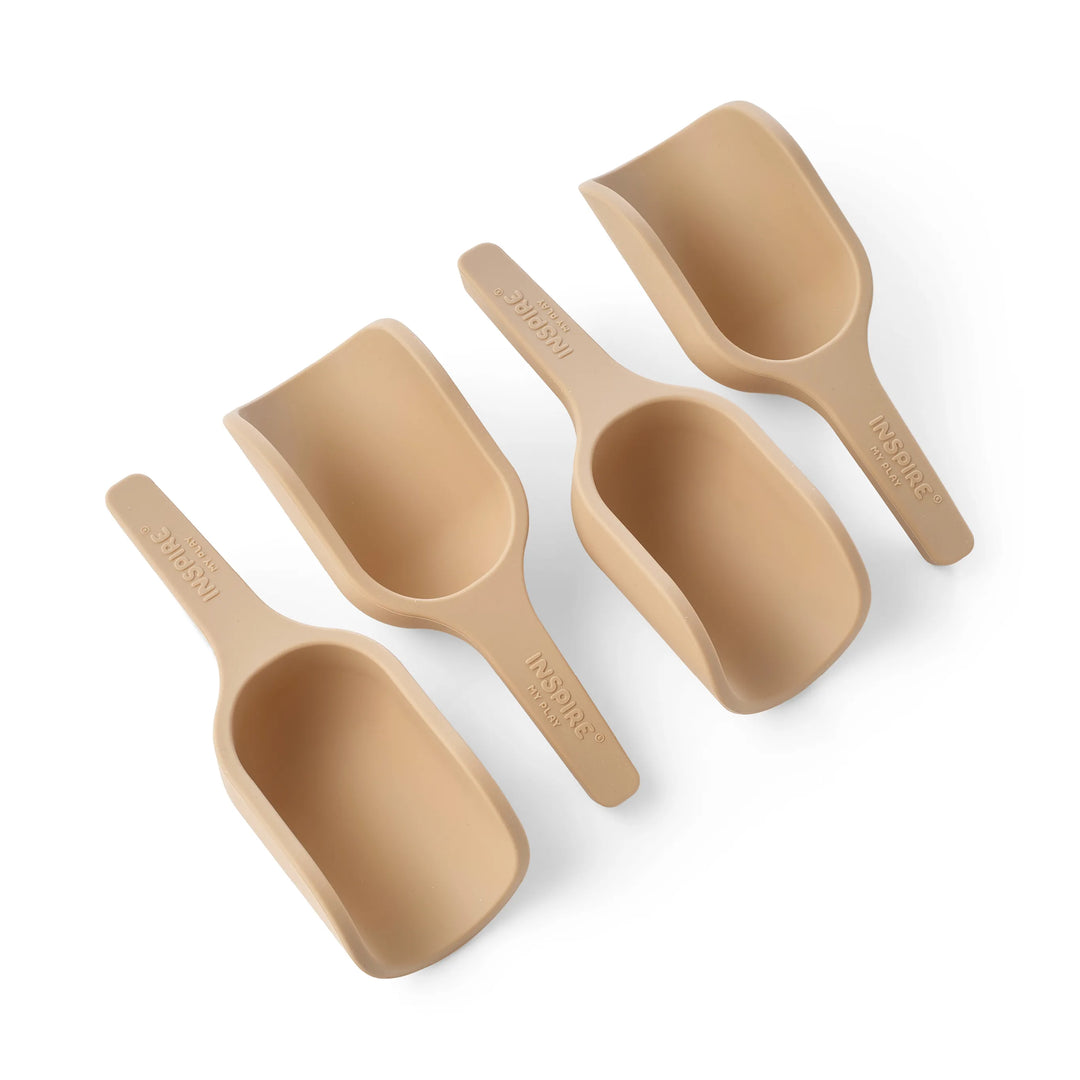 Four mini beige-coloured silicone scoops for sensory play, sand play and water play, arranged diagonally on a white background. The handles are embossed with the brand name 'INSPIRE MY PLAY.'