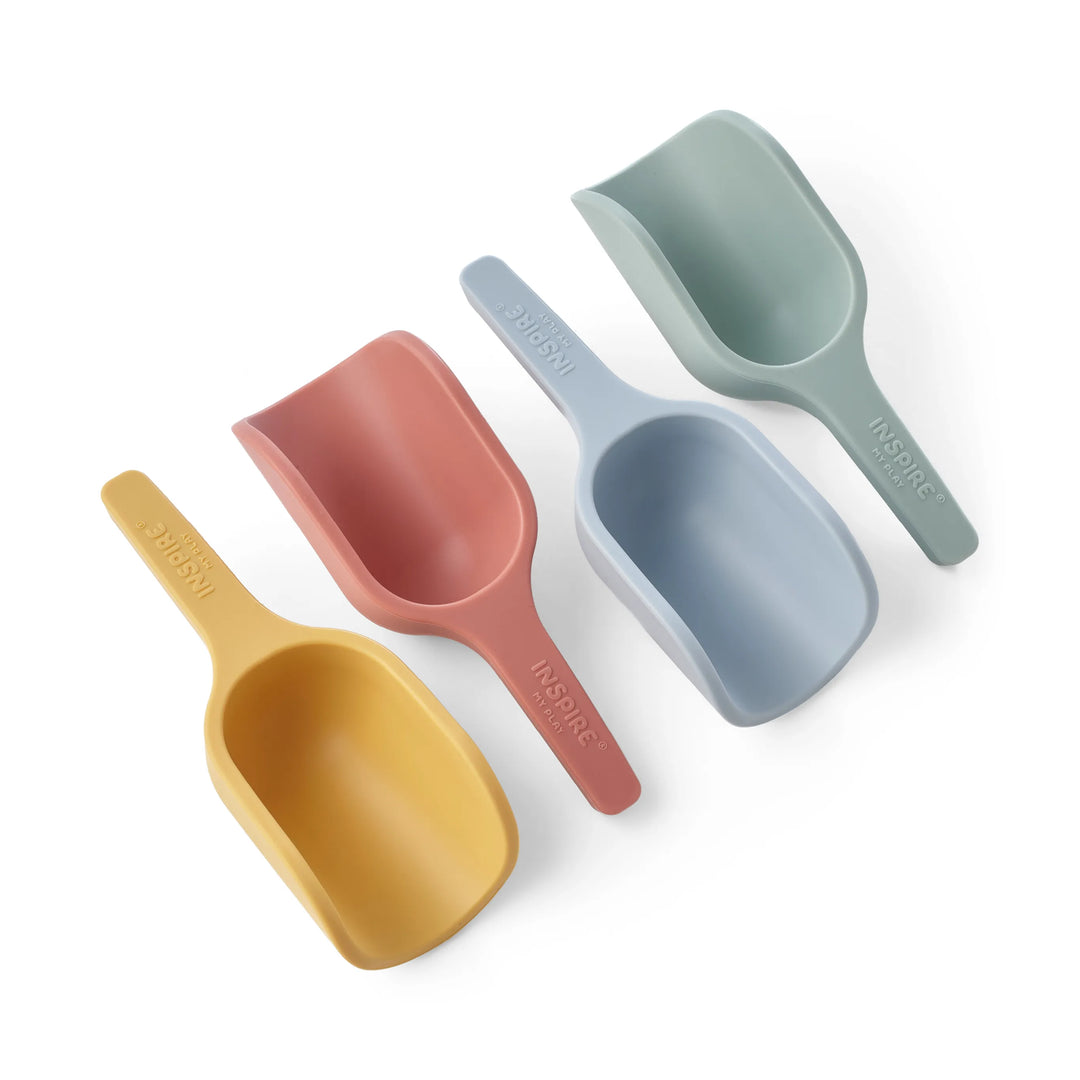 Four mini pastel-coloured silicone scoops for sensory play, sand play and water play in pastel yellow, pink, light blue, and sage green, arranged diagonally on a white background. The handles are embossed with the brand name 'INSPIRE MY PLAY.'
