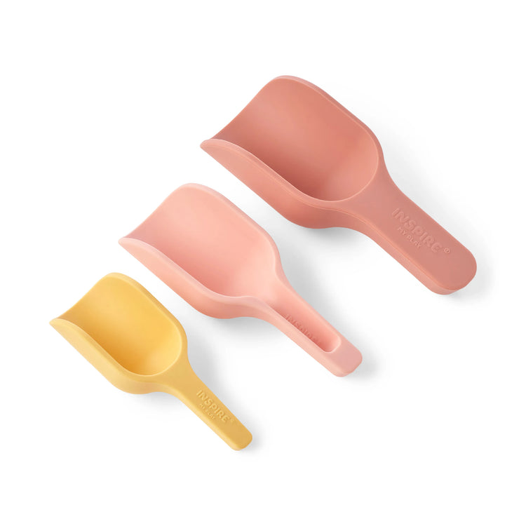Three different sized silicone sensory play nesting scoops in yellow, pale pink and coral arranged diagonally on a clean white background. The brand name 'INSPIRE MY PLAY' is embossed on the handles.