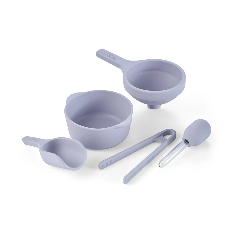 A set of silicone sensory play tools in a light lavender purple colour, including a bowl, scoop, funnel, tongs and dropper, arranged on a clean white background.