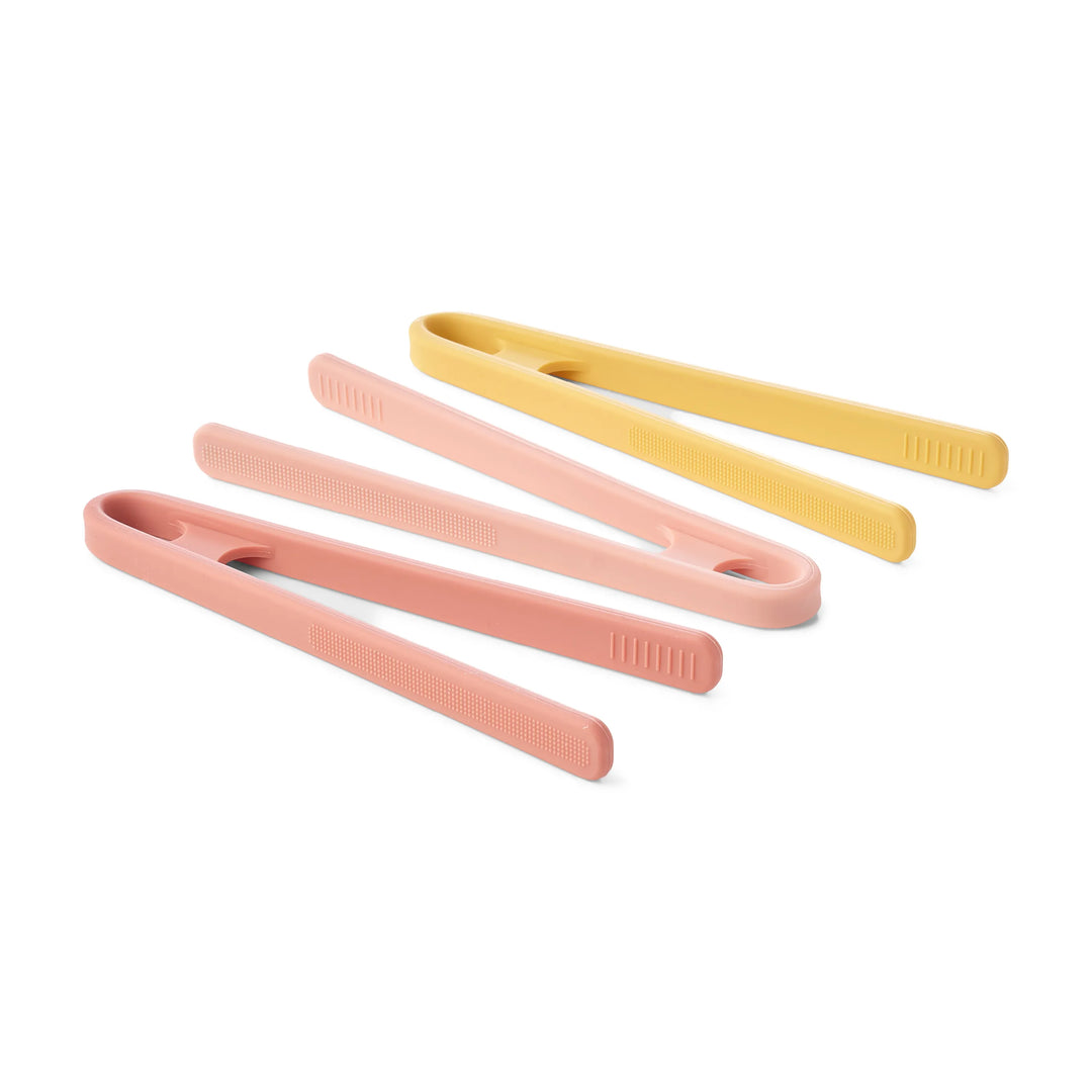 Three pairs of silicone sensory play tongs in pink, peach and yellow, arranged diagonally on a white background.
