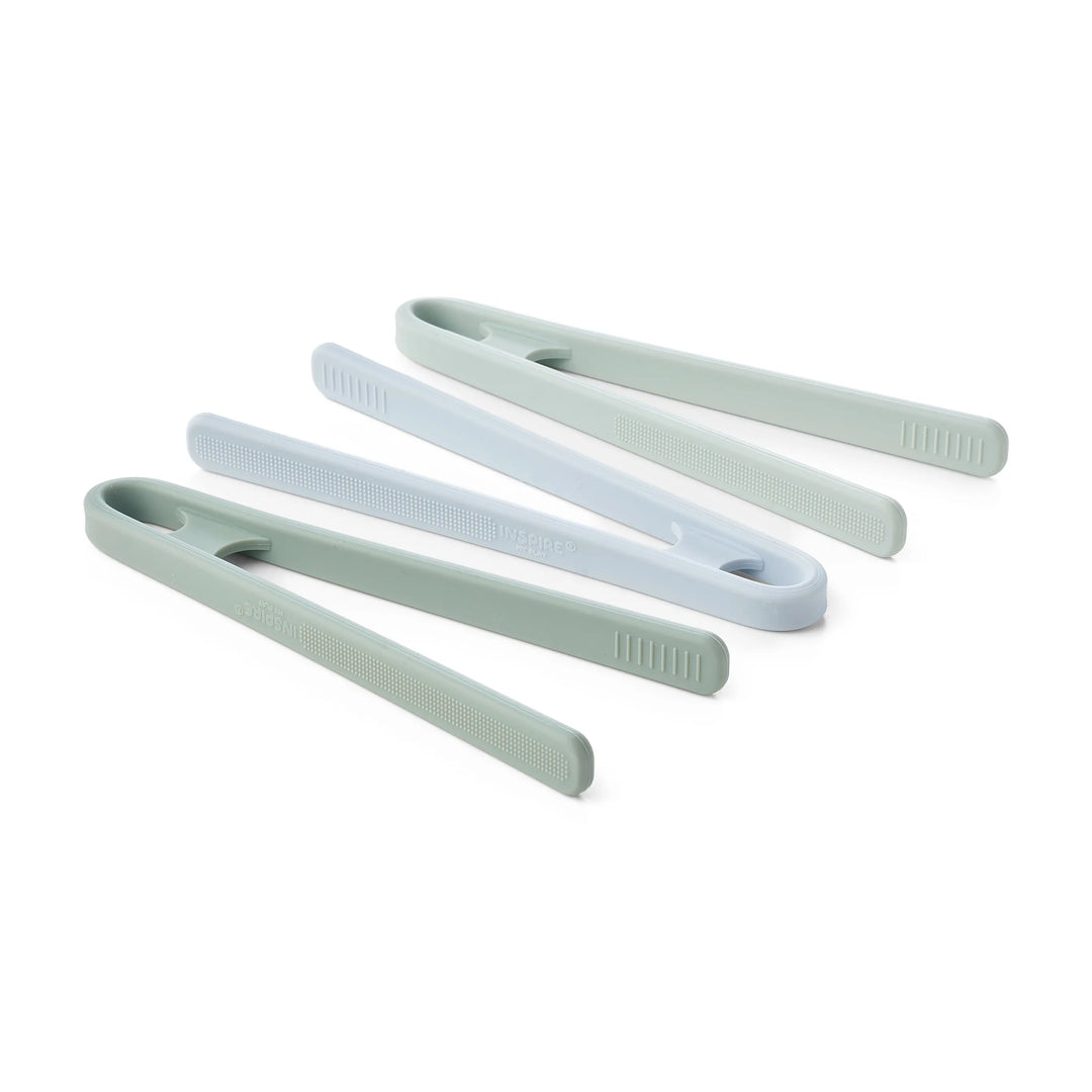 Three pairs of silicone sensory play tongs in sage green, mint green and light blue, arranged diagonally on a white background.