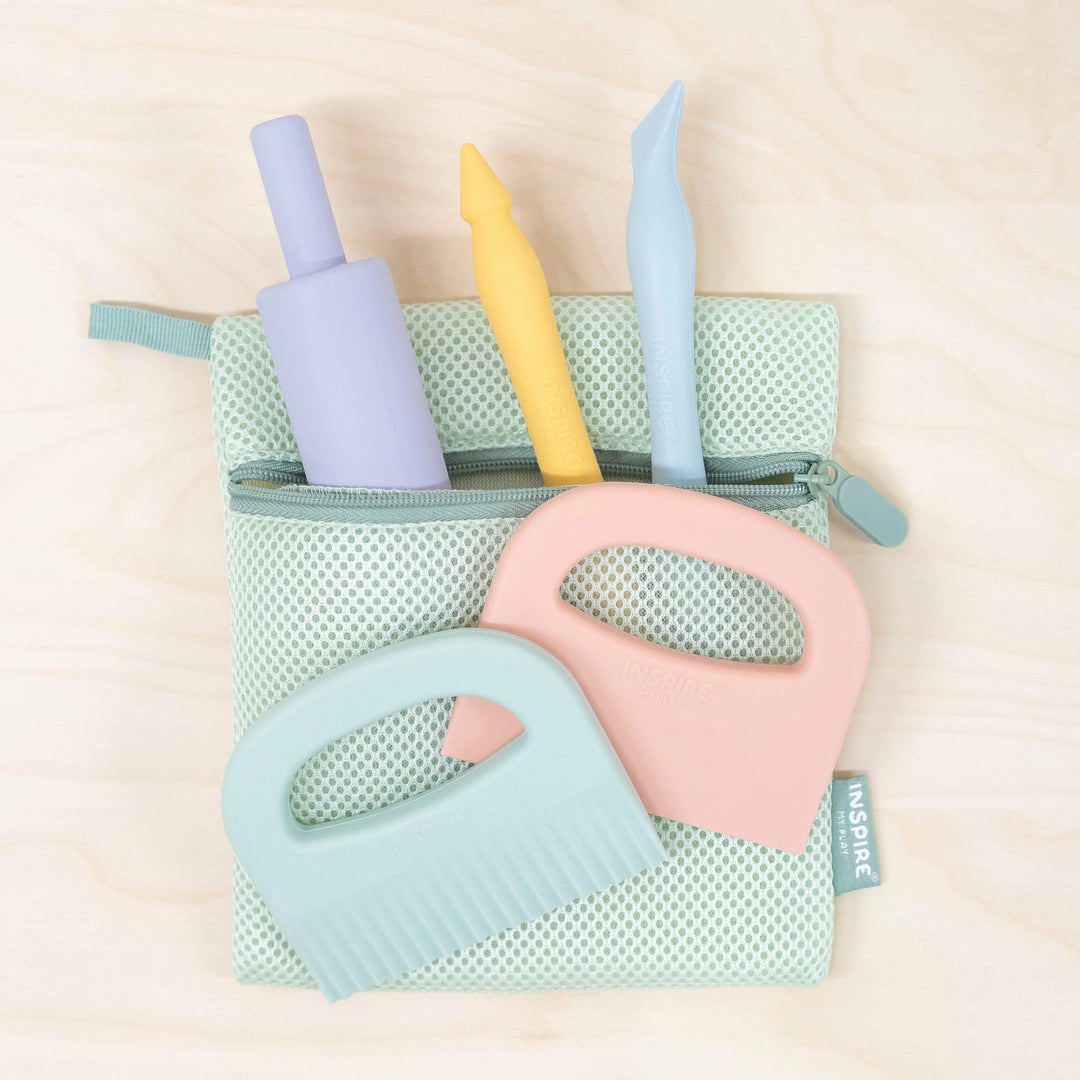Set of colourful pastel playdough tools including a rolling pin, stylus tool, sculpting tool, straight cutter and crinkle cutter in a mesh storage bag.
