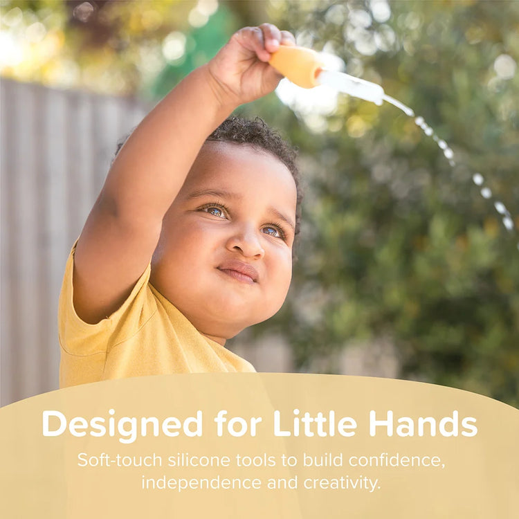 Child squeezing a soft-touch silicone dropper filled with water in the garden with text about how sensory play builds confidence, independence, and creativity.