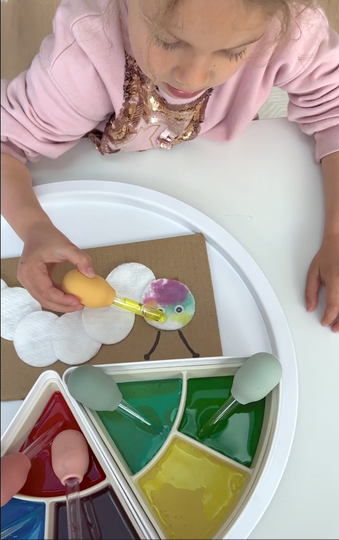 Child using sensory play droppers filled with coloured water to make a cotton wool caterpillar.
