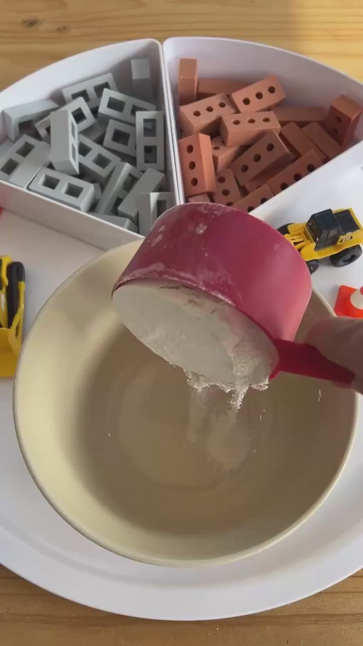 PlayTRAY filled with sensory blocks and bricks and toy diggers with construction sand being mixed in a bowl.