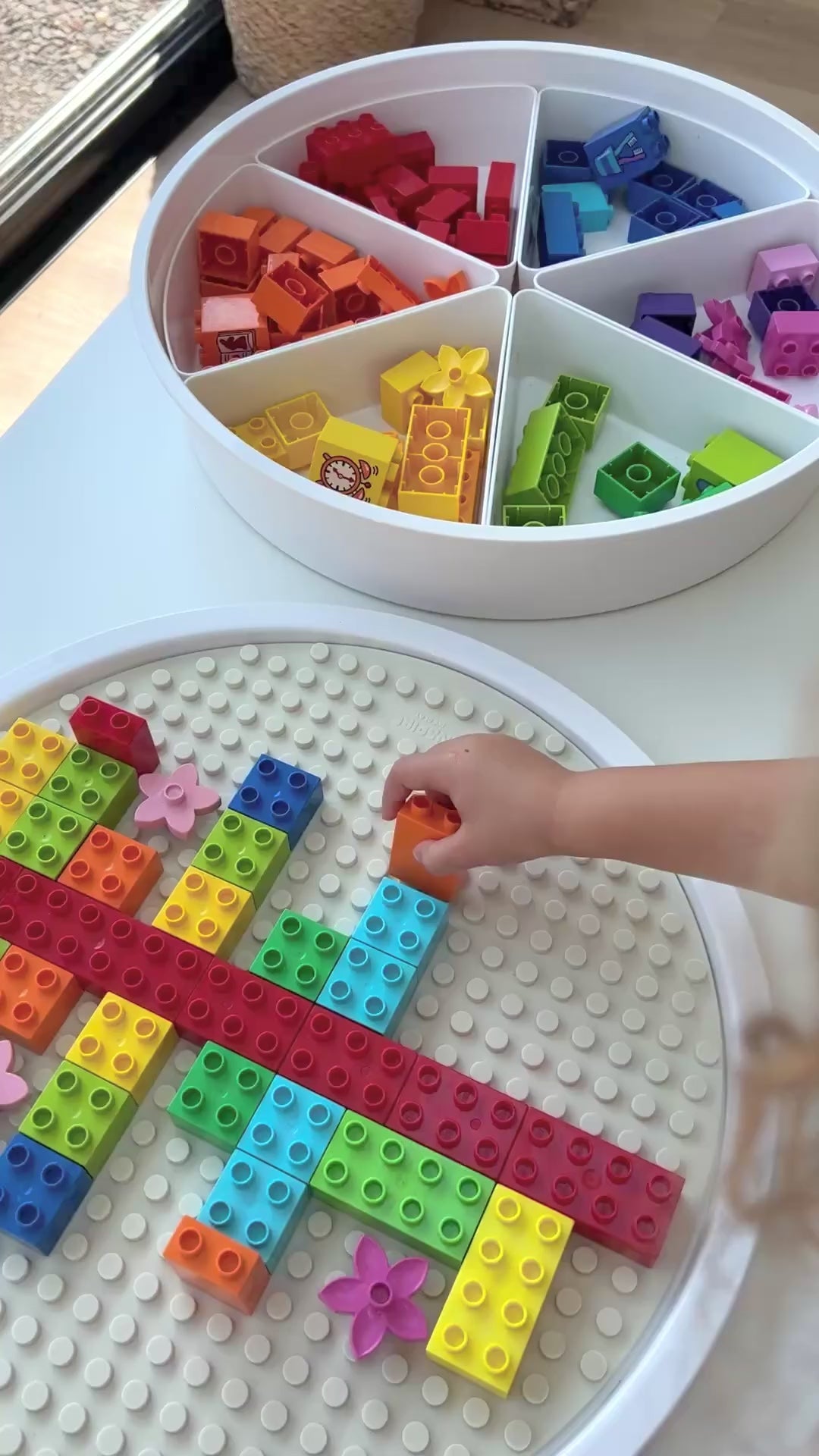 Child placing colourful DUPLO bricks on a silicone building block mat in the lid of the PlayTRAY.