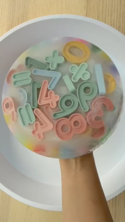 Silicone numbers being retrieved from a block of ice using sensory droppers and tongs.